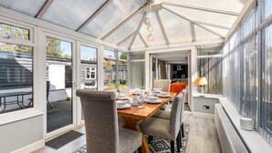 A conservatory with a dining table set for four, large windows, and a view of the outside. - 6-bedroom home for contractors and families. (Colchester)