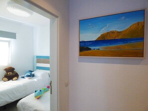 A bedroom with a bed, a teddy bear, a blue whale plush toy, and a painting of a beach scene.