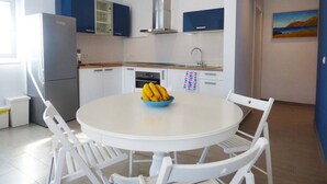 Uma cozinha moderna com armários brancos e azuis, um exaustor de aço inoxidável e uma área de jantar com mesa redonda e cadeiras brancas.