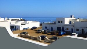 Zona residencial costeira com edifícios brancos, carros estacionados e vista clara para o mar.