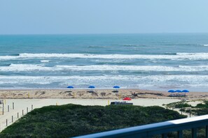 Ein Strand mit Wellen, Sonnenschirmen und blauem Himmel.