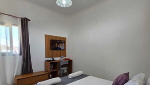 A hotel room with a bed, a desk, a chair, a TV, and a window with curtains.