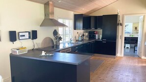Une cuisine moderne dotée d’un grand îlot central, d’appareils électroménagers intégrés et d’un plafond en bois.