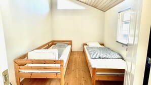 Un petit logement composé d’une seule pièce, avec deux lits superposés en bois, un plafond en pente et une fenêtre laissant entrer la lumière naturelle.