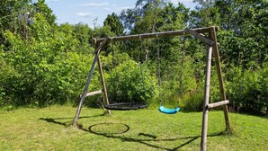 Une balançoire en bois installée dans un espace herbeux, avec des arbres en arrière-plan.