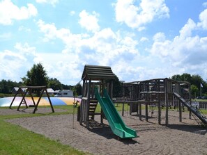 Ein Spielplatz mit einer grünen Rutsche, Schaukeln und einer Kletterkonstruktion.
