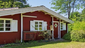 Une maison en bois rouge avec des boiseries blanches, un porche avec un banc, un pot de fleurs et une chaise.