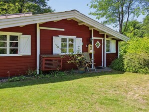 Ein rotes Holzhaus mit weißem Verzierprofil, eine Veranda mit einer Bank, einem Blumentopf und einem Stuhl.