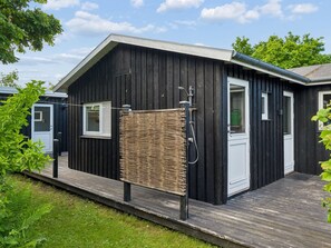 Een zwart houten gebouw met een witte deur, een klein raam en een metalen douchecabine.