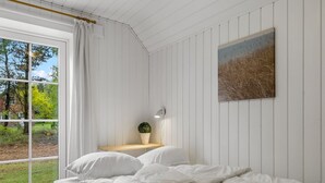 Ein Schlafzimmer mit großem Fenster, einem Bett, einem Nachttisch mit Lampe und einem Bild an der Wand.