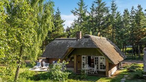 Ein reetgedecktes Häuschen mit Gartenmöbeln, umgeben von Bäumen und viel Grün.