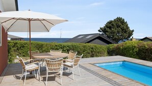 Une terrasse en bois avec une piscine, du mobilier d’extérieur et une vue sur la mer.