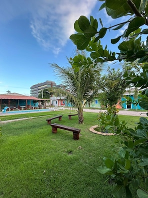 A grassy area with benches, a pool, and buildings in the background. - Pousada Villa Japa (Maragogi)