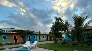 A swimming pool with a dolphin-shaped water feature, surrounded by a patio area with lounge chairs and a grassy lawn. - Pousada Villa Japa (Maragogi)