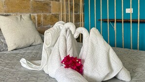 A hotel room with a brick wall, a teal accent wall, a bed with a patterned bedspread, and a towel rack with towels. - Pousada Villa Japa (Maragogi)
