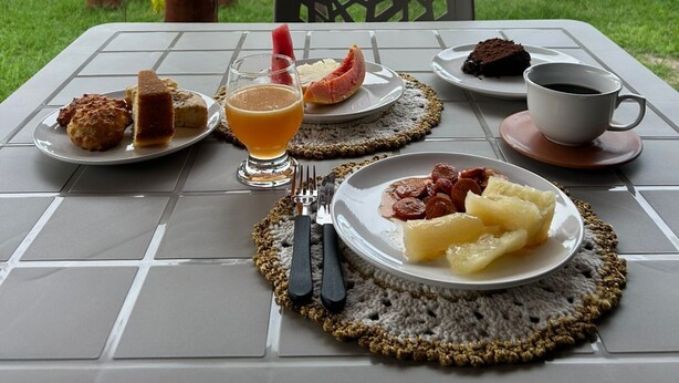 An outdoor dining area with a table set for breakfast, including plates of food, a glass of juice, and a cup of coffee. - Pousada Villa Japa (Maragogi)