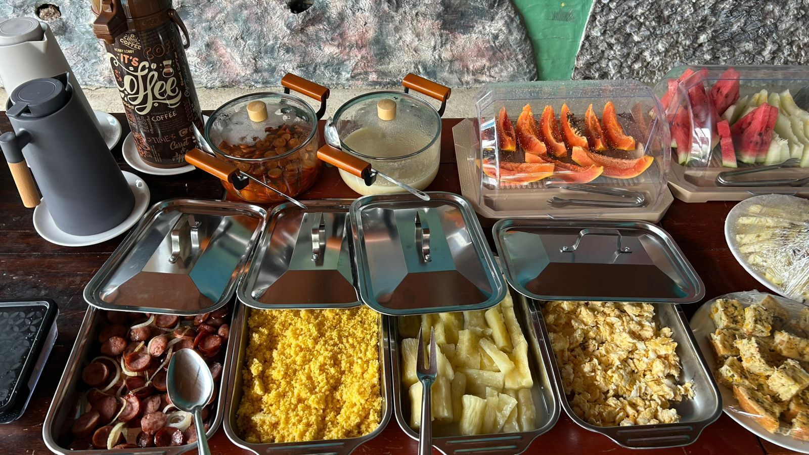 Uma mesa de buffet com diversos alimentos e um espaço para café.