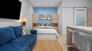Ein modernes Schlafzimmer mit einem Bett, einem blauen Sofa, einem Fernseher und einem Schreibtisch mit Stuhl.