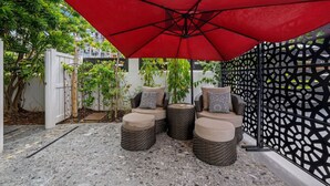 Eine Terrasse mit Gartenmöbeln, einem roten Sonnenschirm und einem dekorativen Zaun.