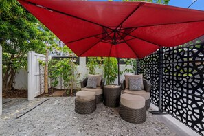 Eine Terrasse mit Gartenmöbeln, einem roten Sonnenschirm und einem dekorativen Zaun.
