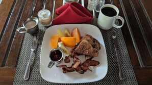 A breakfast plate with fruits, bacon, and coffee on a wooden table. - La Sagesse Bay View (St. David)