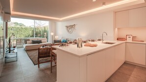 A modern kitchen with a central island, a dining area with a sofa, and a large window providing a view of the outdoors. - FLH Vilamoura Boho Apartment with Terrace (Vilamoura)