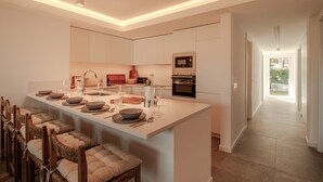 A modern kitchen with a central island, built-in appliances, and a dining area with chairs. - FLH Vilamoura Boho Apartment with Terrace (Vilamoura)
