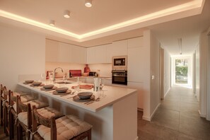 A modern kitchen with a central island, built-in appliances, and a dining area with chairs. - FLH Vilamoura Boho Apartment with Terrace (Vilamoura)