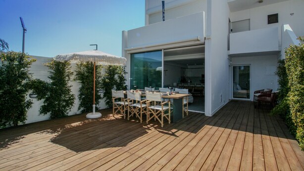 A modern two-story building with a wooden deck, outdoor seating, and a glass door entrance. - FLH Vilamoura Boho Apartment with Terrace (Vilamoura)