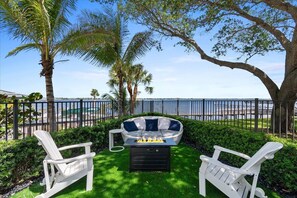 A patio with two Adirondack chairs, a fire pit, and a view of the ocean.