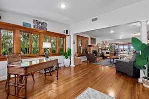 A spacious living room with wooden floors, large windows, and a fireplace.
