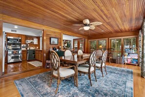 A dining area with a wooden ceiling, a ceiling fan, and a dining table surrounded by chairs.