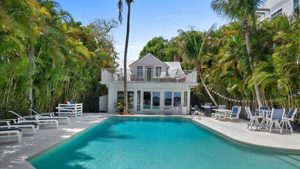 Ein Pool mit Liegestühlen, ein Gebäude mit Balkon und Palmen.