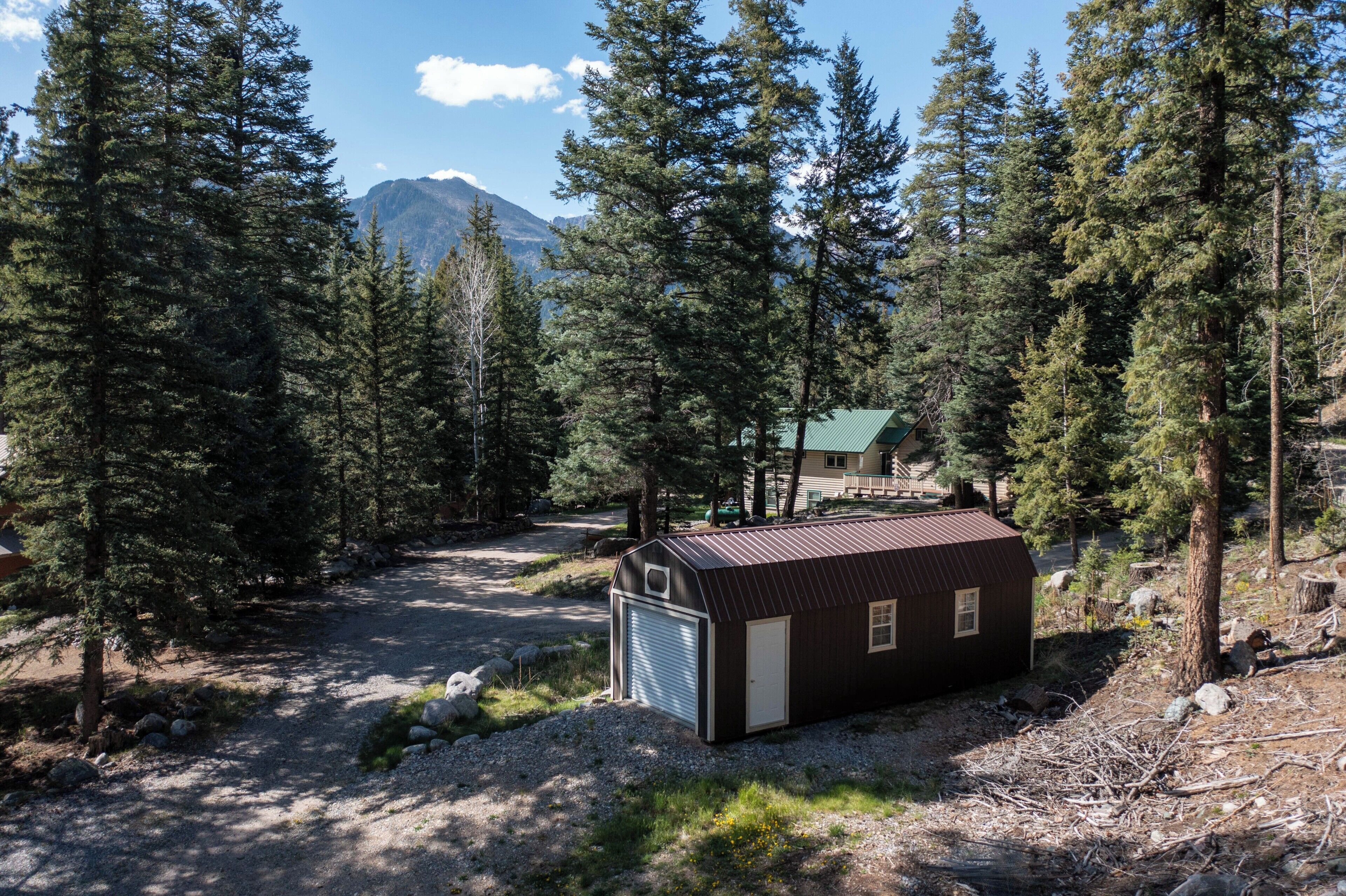 A small cabin with a metal roof, surrounded by dense forest and a mountain in the background.