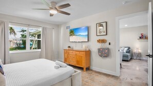 Quarto com cama, ventilador de teto, televisão, armário de madeira e vista para o exterior.