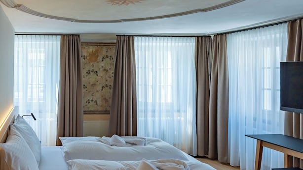 Ein Hotelzimmer mit einem großen Bett, einem Schreibtisch mit Stuhl, einem Fernseher und einem Fenster mit Vorhängen.