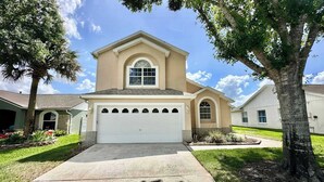 A single-story house with a garage, a central arched window, and a small front yard with a tree and flower beds. - Sunlit Fun Lanai with Pool (Kissimmee)