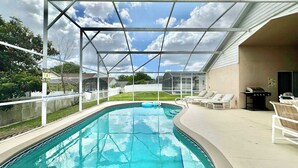 A swimming pool with a covered area, lounge chairs, and a barbecue grill. - Sunlit Fun Lanai with Pool (Kissimmee)