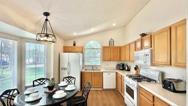 A modern kitchen with wooden cabinets, a white refrigerator, a microwave, a stove, and a dining table set with plates and a potted plant. - Sunlit Fun Lanai with Pool (Kissimmee)