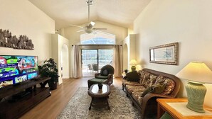 A living room with a television, a sofa, a chair, a table, and a ceiling fan. - Sunlit Fun Lanai with Pool (Kissimmee)