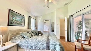 A bedroom with a bed, a nightstand, a lamp, a ceiling fan, a painting, and a sliding glass door leading to a balcony. - Sunlit Fun Lanai with Pool (Kissimmee)