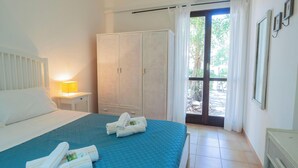 Une chambre d’hôtel avec un lit, une table de chevet avec une lampe, une armoire et une porte donnant sur l’extérieur.