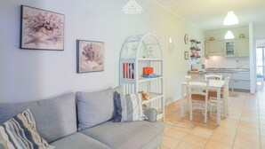 Un salon comprenant un canapé, une table basse et une bibliothèque. Il y a également un coin cuisine avec une table à manger et des chaises.