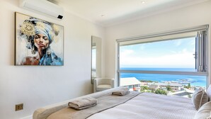 Ein Schlafzimmer mit einem großen Bett, Meerblick, einem Bild an der Wand und einem Fenster.