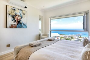 Ein Schlafzimmer mit einem großen Bett, Meerblick, einem Bild an der Wand und einem Fenster.