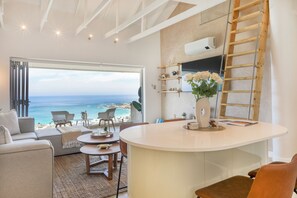 Ein modernes Wohnzimmer mit großem Fenster zum Meer, einem weißen runden Tisch und einer eingebauten Leiter.
