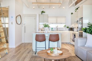 Eine moderne Küche mit einer zentralen Kochinsel, zwei braunen Stühlen, einem Holztisch und einem grauen Sofa.