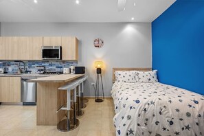 Ein gemütlicher Raum mit einer Küchenzeile, einem Bett mit sterngestrickter Bettdecke und einer blauen Akzentwand.