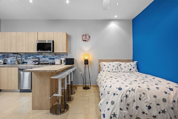 A compact room with a kitchenette, a bed with a star-patterned duvet, and a blue accent wall. - Quiet studio by the beach (San Juan)