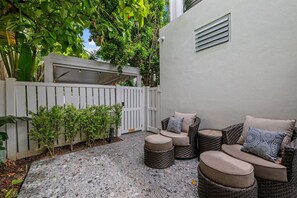 Eine Terrasse mit Korbmöbeln, einem weißen Zaun und einem Gebäude mit einem Fenster.